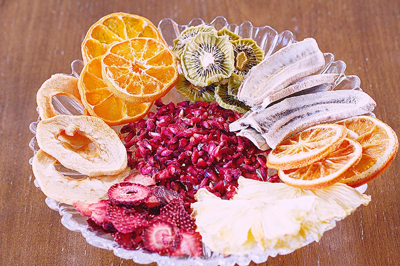 Bir tabakta Frutti Foods'un kurutulmuş meyve çeşitleri: portakal, mandalina, kivi, muz, nar, çilek ve ananas